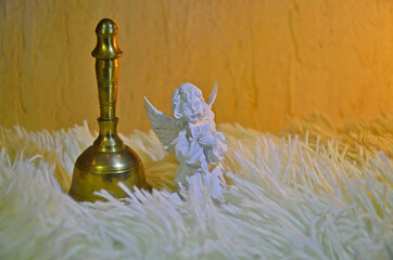 Angel with a Bible. Golden bell. Fluffy bedspread. Yellow background. 