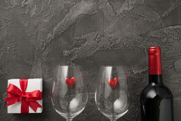 Top view photo of st valentine's day decorations two wineglasses with small hearts white giftbox with red bow and wine bottle on isolated textured dark grey concrete background with empty space