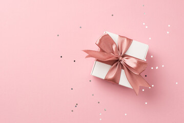 Top panoramic view photo of valentine's day decorations white giftbox with pink satin ribbon bow and shiny sequins on isolated pastel pink background with blank space