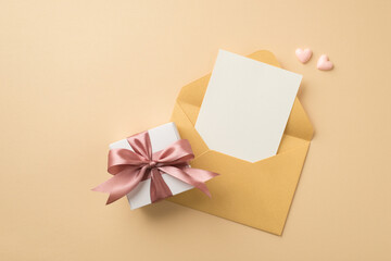 Top view photo of open pastel yellow envelope with card small pink hearts and white giftbox with light pink ribbon bow on isolated beige background with copyspace