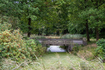 Ein Graben bedeckt mit Entengrütze fließt unter einer Brücke hindurch im Schlossgarten Lütetsburg