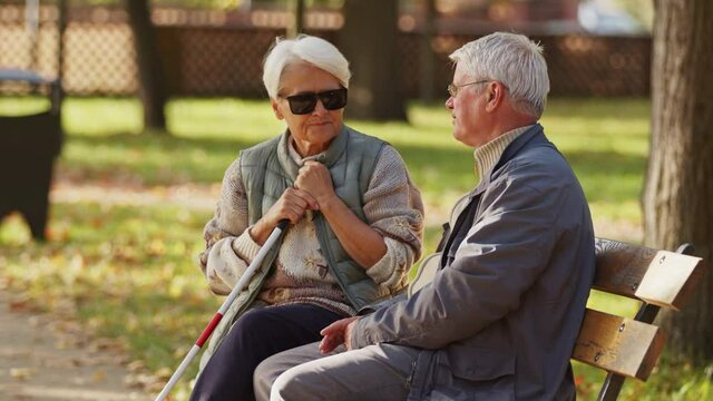 Blind elderly woman sitting on the bech with her husband. An elderly retired couple supporting each other. High quality 4k footage