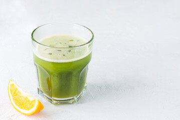 A cold drink made from matcha and orange juice with ice in a glass on a light table. Horizontal orientation, copy space.