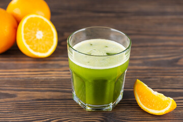 Cold drink from matcha and orange juice with ice in a glass on a wooden table.