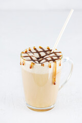 Caremel latte macchiato with coconut milk in a glass mug on a light table.