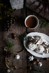 Meringue cookies with chocolate and almond cream and cup of hot chocolate, wrapped presents and natural winter decorations on old wooden table 