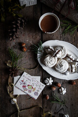 Meringue cookies with chocolate and almond cream and cup of hot chocolate, wrapped presents and natural winter decorations on old wooden table 