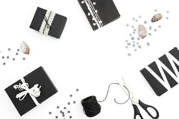Christmas frame of stylish black gifts with twine, silver cofetti and scissors on white background. Winter concept. Flat lay