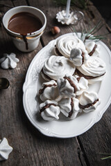 Meringue cookies with chocolate and hazelnut cream and cup of hot chocolate, wrapped presents and natural winter decorations on old wooden table 