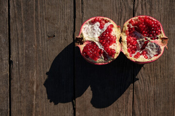Broken pomegranate on a wooden surface. Bright sun. Hard shadows. Top view. Copy space. 