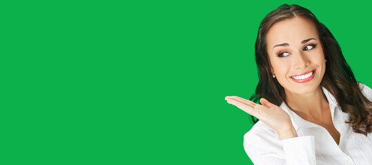 Happy smiling woman in white confident blouse giving, holding or showing something or copy space for some text. Business concept. Green colour background. Brunette businesswoman. Wide image