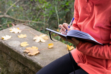 Unrecognizable woman writing in notebook in nature