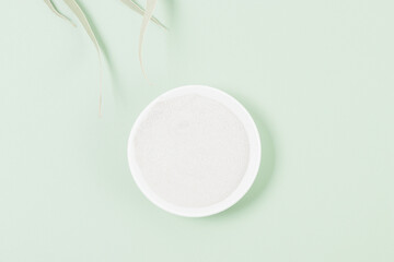 Cosmetic clay powder in bowl on green background