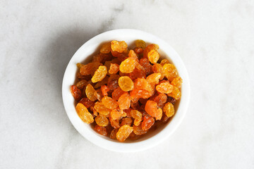 A top view image of yellow seedless raisins in a white ceramic bowl. 