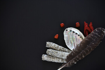 A top view image of white sage smudge sticks and abalone shell on a black background. 