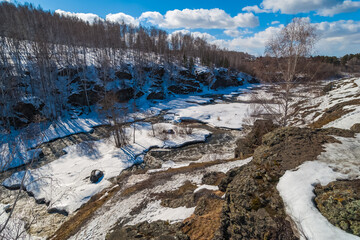 Spring landscape with river, rocks, ice, snow, trees and blue sky with white clouds
