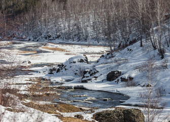 Fast river, rocks, ice, snow, trees, shrubs, dry grass in spring