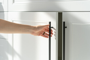 Woman's hand holding on handle of kitchen cabinet - obrazy, fototapety, plakaty