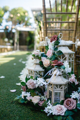 Wooden chairs in a row decorated with fresh pink and white roses with greenery for the wedding ceremony outdoors White lantern on the ground decorated with flowers Cropped photo Close up