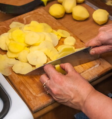 Women's hands cut potatoes with a knife on a wooden board close-up