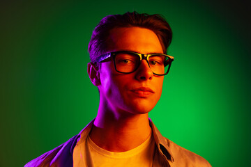Handsome young serious man looking at camera isolated on green studio background in neon, monochrome.