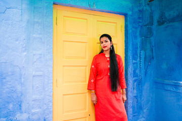 Beautiful Indian female model at blue district of the old city in Jodhpur, Rajasthan, India. Hindu girl with long hair, tilak and traditional Indian red kurta in front of yellow door.