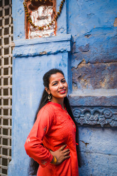 Beautiful Indian female model at blue district of the old city in Jodhpur, Rajasthan, India. Hindu girl with long hair, tilak and traditional Indian red kurta next to a Ganesh statue. 