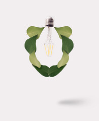 Light bulb shape formed with green leaves floating over the white background. Clean electricity minimal concept.