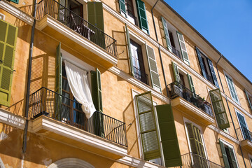 Balconies and windows in different green hues at an orange facade of mediterranean house © Florian Guenther/Wirestock