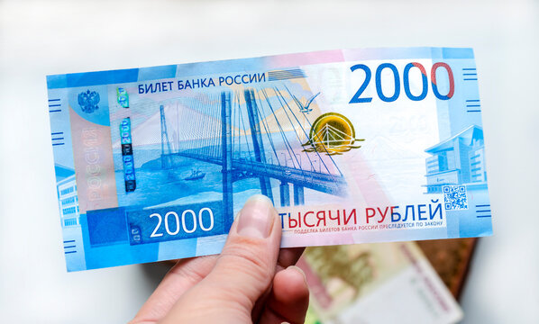 A Russian banknote with a face value of 2000 rubles in the hand of a woman against the background of a brown wallet with other banknotes. The concept of finance, investment, savings and cash.