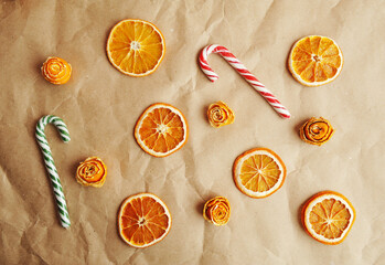 Dried orange slices, roses made of tangerine peel and candy canes on craft paper. Christmas concept background