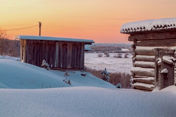 Old wooden sheds on a snow-covered hill. Rural winter landscape