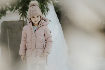 Mädchen in Winterjacke mit Haube steht vor Iglu