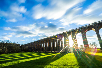 The sun shining through one of the arches at Ouse Valley Viaduct as the clouds stream overhead.