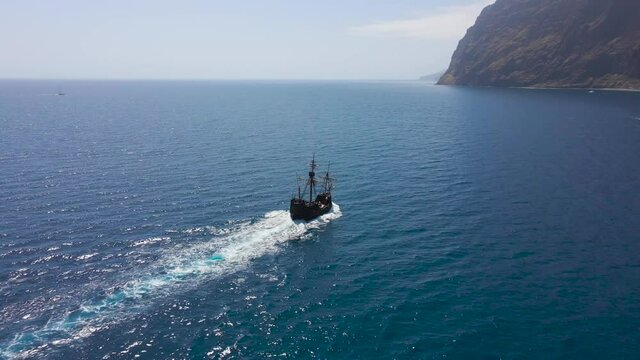 The pirate ship Santa Maria de Colombo sails off the coast of Madeira - 4k drone shot. Atlantic sea with cliffs in the background.
