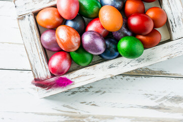 Easter multicolored eggs in a homemade wooden box on a white wooden table. top view. a copy space. the concept of the Easter holiday.
