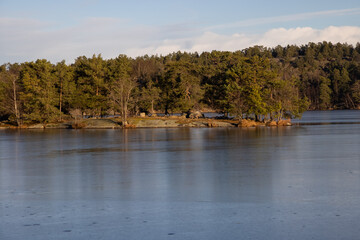 Beautiful natural Scandinavian landscape. Frozen lake with forest and stones at the shore line. Sunny late autumn or winter day in the nature in Sweden. Real is beautiful