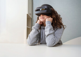 Teen girl wearing Virtual Reality headset is experiencing VR sitting at desk home.