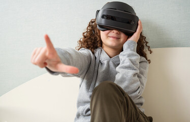 Teen girl wearing Virtual Reality headset is experiencing amazement VR sitting on bed home.