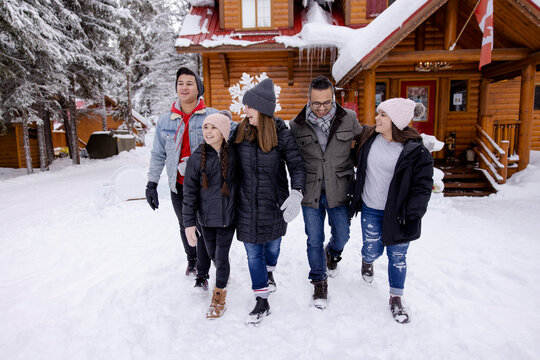 Happy Family Walking In Snow Outside Winter Resort Cabin