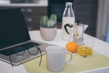 Table set for breakfast, kitchen in the background. Natural meal and technology devices. Interior view of a cozy and modern home. Millennial, youth, home working, home schooling, remote work concept.
