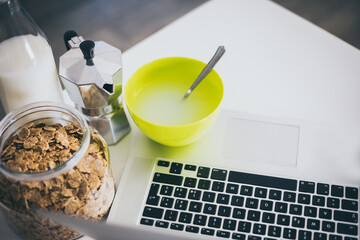 Table set for breakfast, kitchen in the background. Natural meal and technology devices. Interior view of a cozy and modern home. Millennial, youth, home working, home schooling, remote work concept.