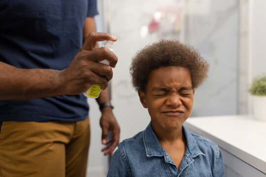 Father spraying afro on son with closed eyes