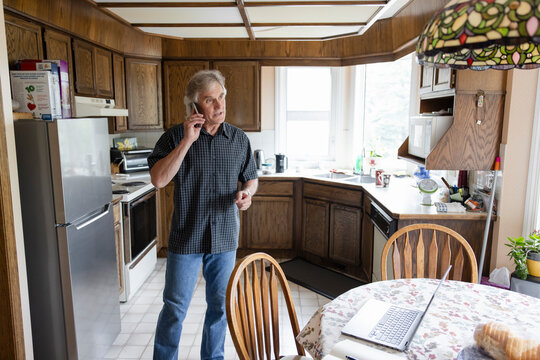 Senior Man Talking On Smart Phone In Kitchen