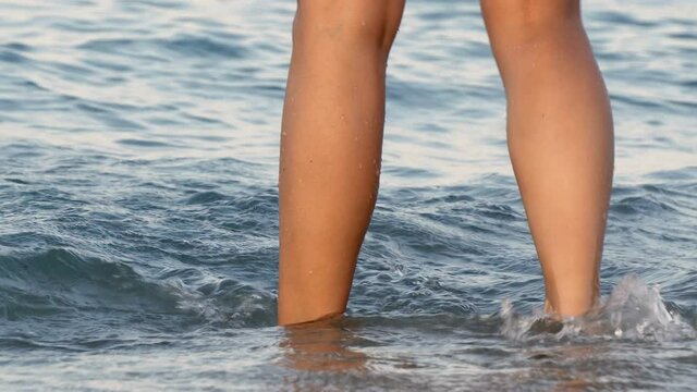 Female legs close up splashing in the sea's waves in the beach