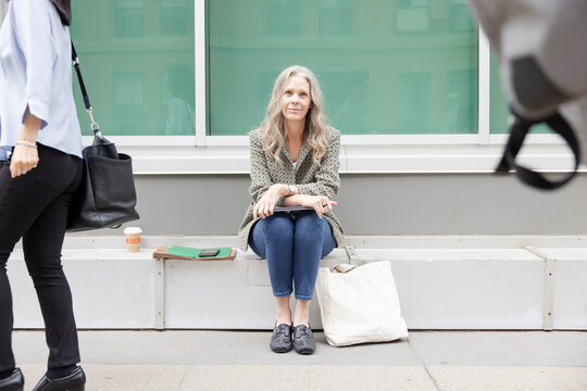 Portrait of cheerful businesswoman sitting on sidewalk