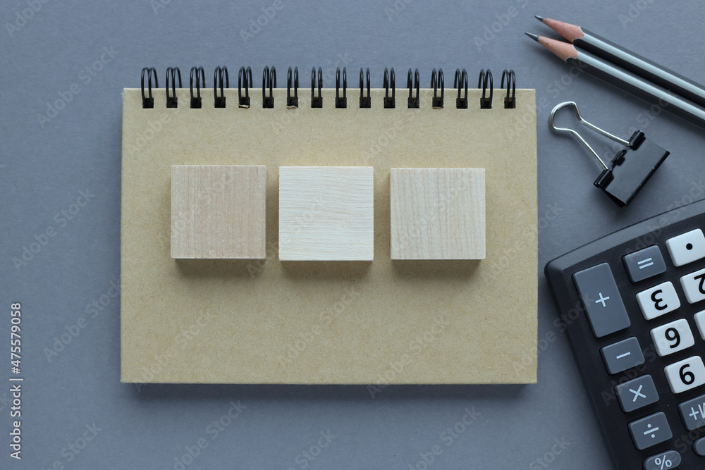 Aufkleber 3 wooden blocks on notepad top view on gray background near calculator and notepad