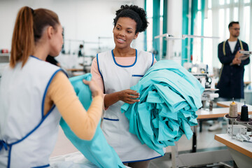 Fototapeta premium Young African American seamstresses talks with Caucasian coworker while working in textile factory.