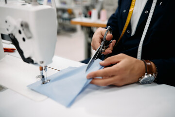 Close-up of production line worker cuts fabric while working in sewing factory.