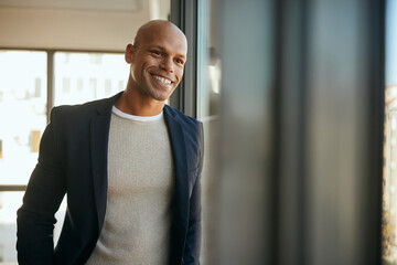 Happy black entrepreneur looks through the widow while working in office.
